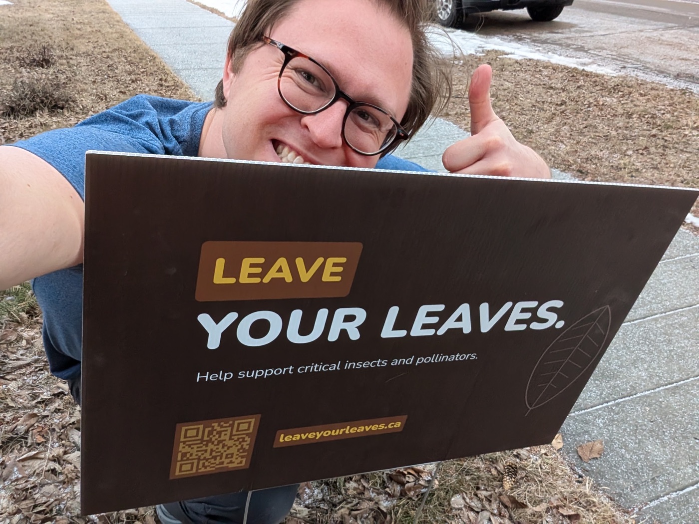 Troy giving a thumbs up behind a brown Leave Your Leaves yard sign on a leaf-covered lawn